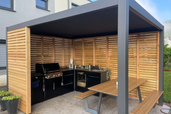 Masa cu bancute si bucatarie modulara de exterior BBQ KItchen pe terasa acoperita, langa cladire.
